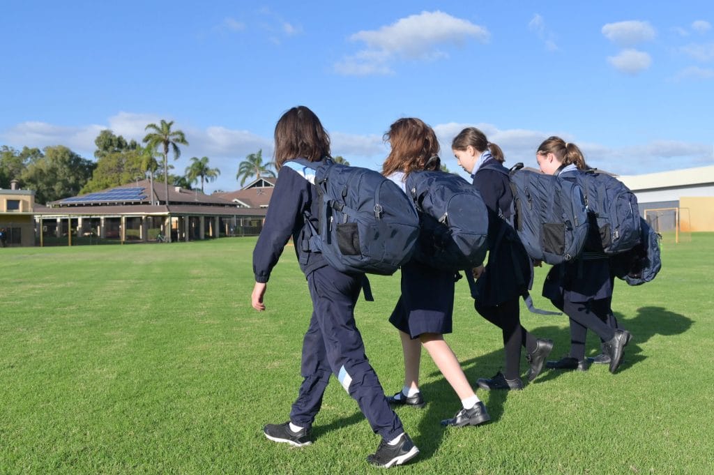 Four students in school uniform with backpacks walking across a school oval in Bendigo, Victoria on a sunny day.