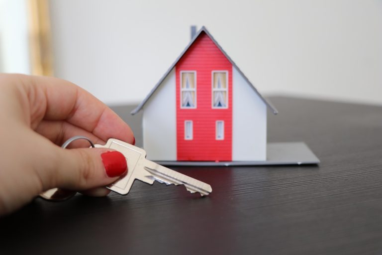 Hand holding house keys next to a red model home, symbolising buying property in Tarneit VIC 3029