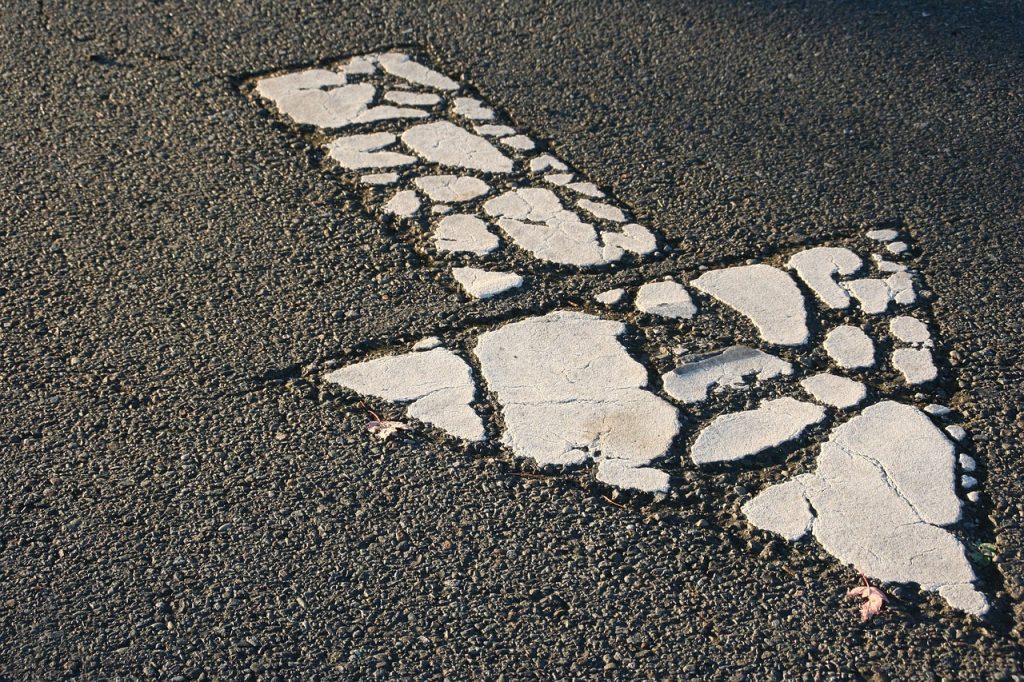 Close-up of a worn white downward road arrow on asphalt