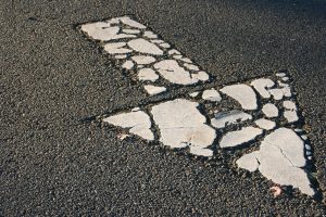 Close-up of a worn white downward road arrow on asphalt