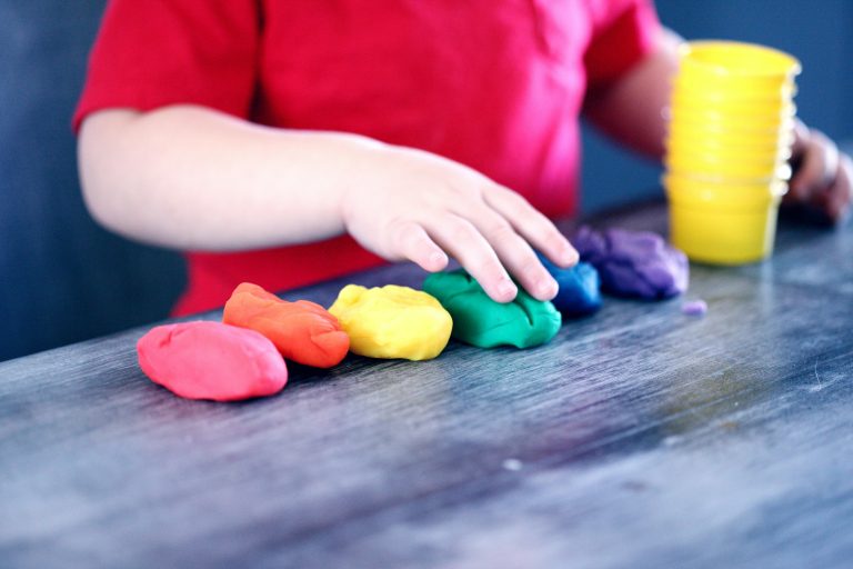 A young child playing with rainbow-coloured playdough at a table, representing early learning and childcare in Ballarat, Victoria.