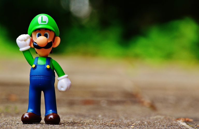 Luigi figurine standing on outdoor pavement with a blurred green background.