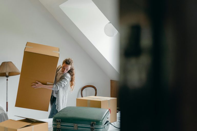 Woman carrying moving box in bright living room, preparing to relocate to a new home in Southport on the Gold Coast
