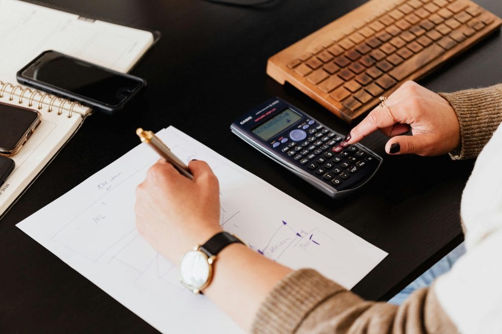 Close-up of a person using a calculator and laptop to review financial documents at a desk.