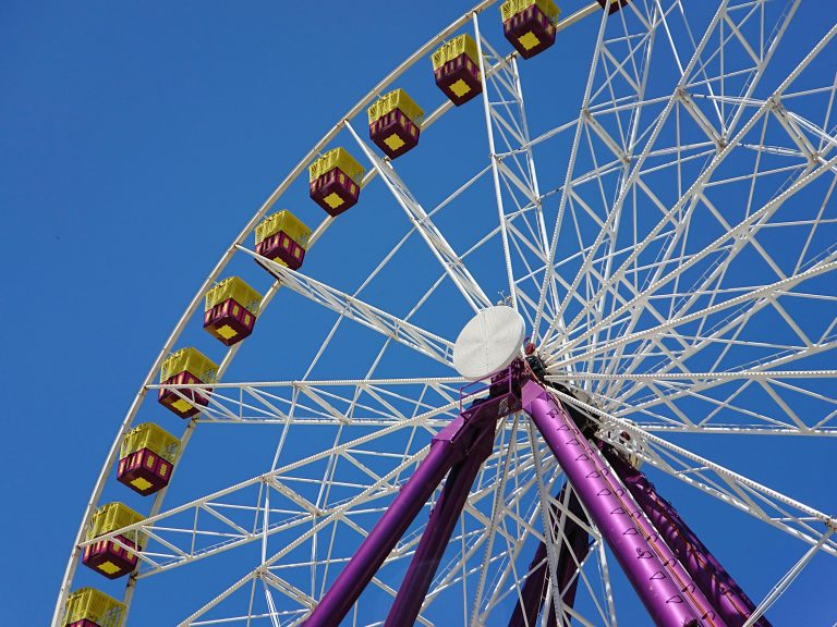 Geelong waterfront ferris wheel viewed from below, with purple supports and yellow gondolas against a clear blue sky.